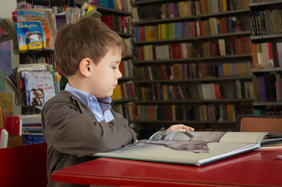 Gutt som sitter ved et rødt bord i et bibliotek og leser.