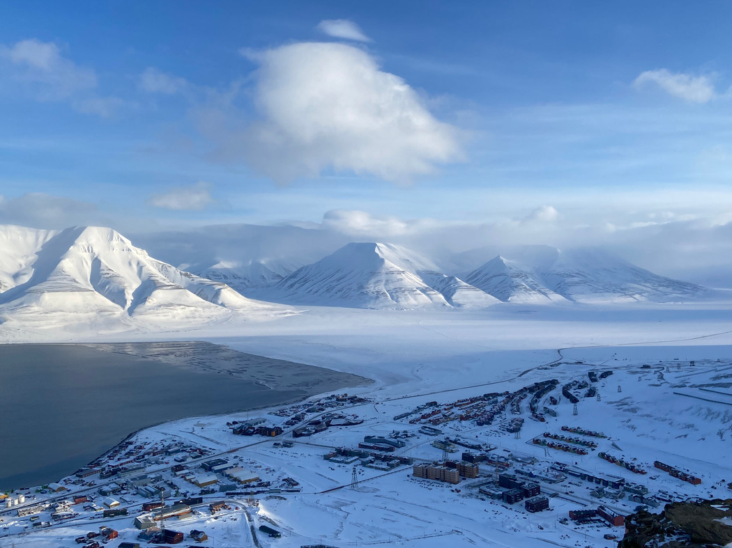 Landskapsbilde fra Svalbard med en vik, snødekte fjell og bebyggelse.